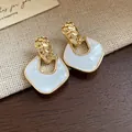 Primo piano di orecchini stile palazzo retrò con trama dorata e ciondolo a rombo bianco - Stile Rombo Martellato (HE28821) / Bianco