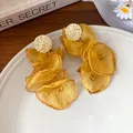 Detailed view of yellow chiffon petal tassel earrings with hammered gold studs on a plate. - Yellow