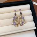 Nahaufnahme von quadratischen Vintage-Ohrringen mit lila Glaskristallen auf beigem Tablett - Unregelmäßige Geometrische Ohrringe / Gold-Lila