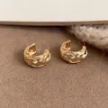 Primer plano detallado de pendientes en C dorados con una elegante textura cruzada tejida - Grande / Dorado