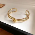 Primo piano di un bracciale a polsino dorato minimalista con design a nodo intrecciato - Stile Nodo a Doppia Linea / Oro