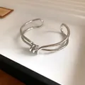 Primo piano di un bracciale rigido argento ritorto irregolare con dettaglio a nodo - Stile Nodo a Doppia Linea / Argento