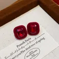 Macro view of red flocked geometric stud earrings resting on a jewelry box label - Square Rhinestone Flocked Style (HE30500) / Red