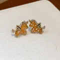 Nahaufnahme von goldenen Einhorn-Ohrsteckern mit orangefarbenem Kristalleinsatz und Zirkonia - Silberstift Einhorn Stecker / Vergoldet Kaffee