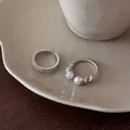 Close-up of silver-toned zircon and pearl textured adjustable open rings on a ceramic plate. - Two-Piece Set / Silver