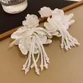 Close-up of white flower petal earrings with long beaded tassels on a leather tray - White