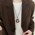 Long collier de style Zen avec pendentif carré marron porté sur un blazer marron. - Collier Pendentif Anneau Géométrique (15#)