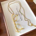 Detailed view of a gold-finish eyeglass pendant necklace on a wooden jewelry tray. - Gold