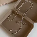 Vista detallada de un collar lariat con lazo plateado y dijes de gotas en una caja marrón. - Plata (15#)
