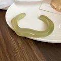 Gros plan d'un jonc en acrylique marbré vert au design ondulé sur une assiette blanche - N°8 Bracelet - Vert Clair