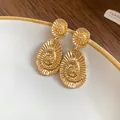 Macro view of gold oval stud earrings featuring elegant spiral texture on white plate. - Oval Spiral Texture Style / Gold