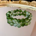 Primo piano dettagliato di un braccialetto di perle di vetro verde sfumato su uno specchio - Perle Tonde Effetto Crepa Sfumate / Verde