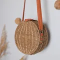 Detailansicht einer runden Stroh-Umhängetasche im Vintage-Stil mit strukturiertem orangefarbenem Gurt - Kaffeebraun