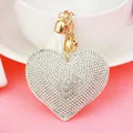 Close-up detail of a heart-shaped keychain with sparkling rhinestones and white tassel - Gold Tone + White Base With Clear Rhinestones