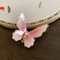Elegant pink iridescent butterfly hair clip with pearl and rhinestone detail on a wooden surface - Pink