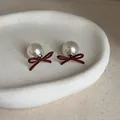 Eleganti orecchini a perno con fiocco bordeaux e perla bianca su piatto di ceramica - Orecchini di Perle con Fiocco