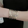 Elegant silver-toned hollow rose pattern wide metal cuff bracelet shown on wrist - Flower Hollow Cuff Bracelet