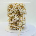 Detail macro of hand-woven white bead flower chain on spool for DIY jewelry making - Gold Ceramic-look PVC White