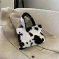 Cute black and white cow print plush handbag for women shown on a beige winter coat - Black Cow Print