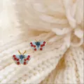 Delicate light blue butterfly stud earrings with red rhinestone accents on white knit - Blue Red Enamel Butterfly (925 Sterling Silver Earring Post)
