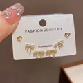 Vista dettagliata di tre paia di orecchini a perno dorati a forma di fiocco e cuore - Set Di Tre Orecchini A Forma Di Cuore Con Fiocco E Strass Placcati In Vero Oro (3# Oro)
