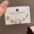 Close-up of elegant small stud earrings set with sparkling stones on display card. - 35# Gold - Fully Diamond Square Three-piece Earring Set (thickened Real Gold Plating)