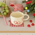 Vista dettagliata di una tazza in ceramica crema con motivi a fiocco rosso in una scena accogliente - 201-300ml / Rosso