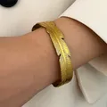Vintage gold feather-shaped stainless steel cuff bangle bracelet shown on woman wrist - Feather Texture (K-353)