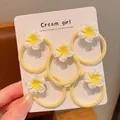 Close-up of five cute yellow frangipani flower hair ties on a white display card. - Small Frangipani Fine Hair Tie