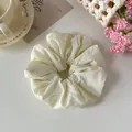 Dettaglio di uno scrunchie in tessuto crema con una morbida trama arricciata. - Beige
