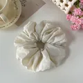 Vista ravvicinata di uno scrunchie in tessuto crema con dettagli di pieghe morbide - Bianco Sporco