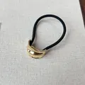 Close-up detail of a minimalist gold metal crescent hair tie on a textured beige fabric background. - Concave Style - Gold
