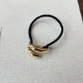 Detail shot of minimalist retro gold metal charm on a durable black elastic hair tie - Wrap Style - Gold