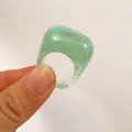Close-up of minimalist green marble acrylic oval ring held between fingers. - Cyan Blue (31761)