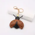 Macro view of a creative brown leather ladybug keychain pendant with golden metal hardware - Brown