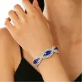 Elegant silver bracelet with oval blue gemstones and clear zircon inlay worn on wrist - Blue Gemstone Intertwined Style (M-285)