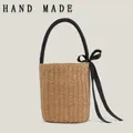 Cylindrical straw woven bucket bag featuring a black top handle and silk ribbon bow detail - Camel