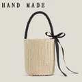 Handmade beige woven straw bucket bag featuring a black handle and a large ribbon bow - Beige