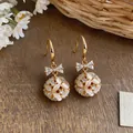 Close-up of elegant 14k gold bowknot earrings with cat-eye stone floral sphere drops - Butterfly Flower Ball Style / Gold