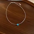 Close-up detail of a silver-toned heart necklace with a blue zircon pendant on a wood surface - Heart Pendant Necklace / Silver-Blue