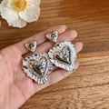 Detailed close-up of vintage silver heart-shaped earrings with ruffled edges on hand - Ruffled Heart (HE33628) / Gold & Silver
