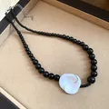 Primo piano di una collana di perle nere con un ciondolo a fiore in smalto bianco in un vassoio - Collana-Nero