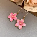 Detail view of pink enamel flower earrings with gold hooks on textured background. - Gold-Pink Hook Style