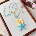 Vue détaillée du collier océan avec étoile de mer bleue, fleur jaune et breloques coquillages. - Bleu-Marron