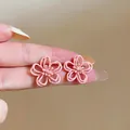 Makro-Detailansicht minimalistischer rosafarbener hohler Blumenohrringe auf dem Finger - Hohle Blume (HE32264) / Rosa
