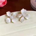 Close-up detail of elegant white flower stud earrings with shimmering frosted finish. - Silver Earring Post Style / White