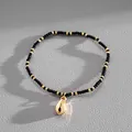 Macro detail of golden cowrie shell charm on black and gold seed bead vacation bracelet - Black-Shell