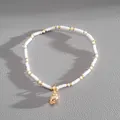 Detailed view of a white seed bead bracelet with a polished golden conch shell charm. - White Conch