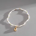 Detail view of white seed bead bracelet with a gold shell pendant on grey texture. - White Shell