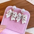 Vista dettagliata di eleganti orecchini a fiocco bianco con perle su scatola rosa - Stile Fiocco (HE34170) / Confezione da 1 paio / Argento